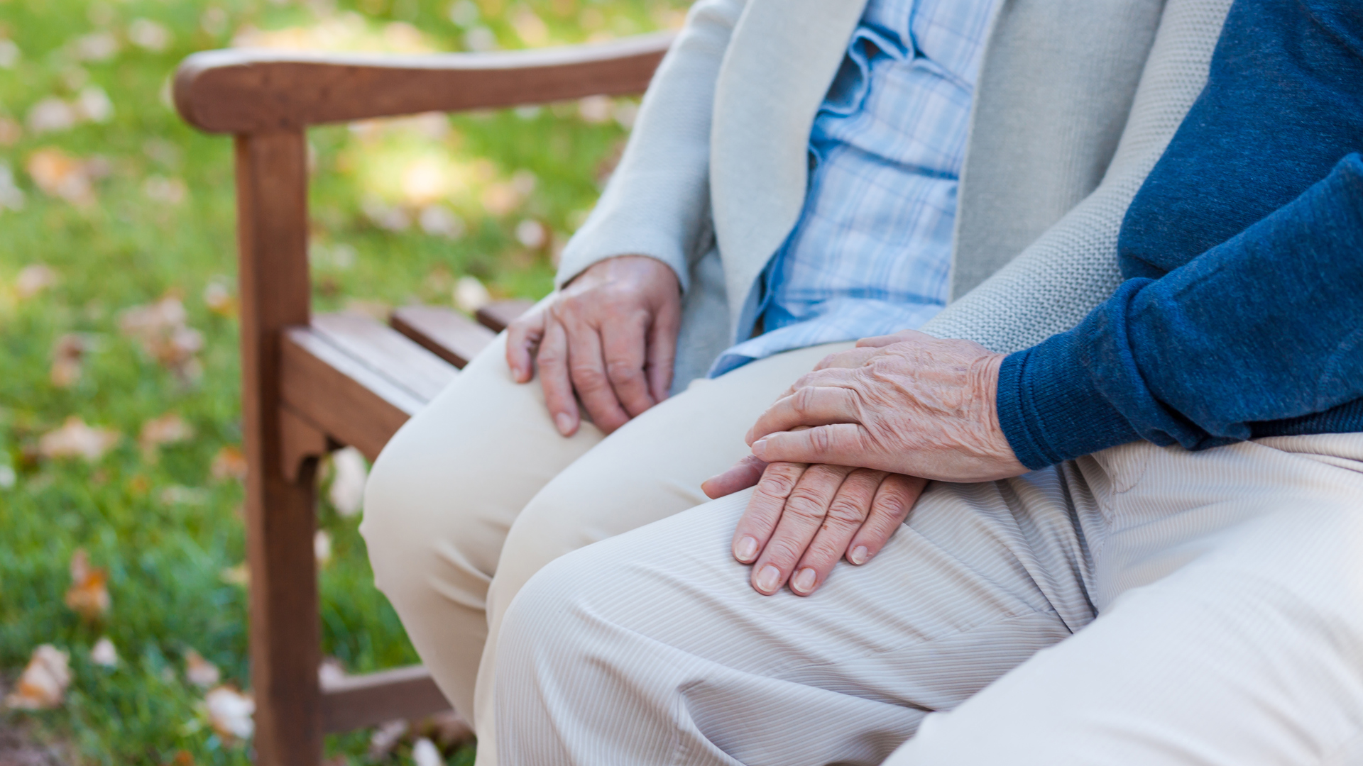 Äldre par håller handen, sitter på en bänk