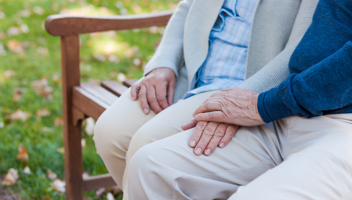 Äldre par håller handen, sitter på en bänk