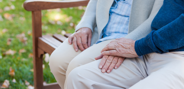 Äldre par håller handen, sitter på en bänk