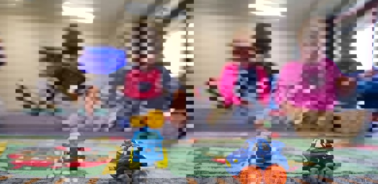 Två leksaksbilar på ett golv med lekande barn i bakgrunden