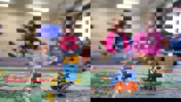 Två leksaksbilar på ett golv med lekande barn i bakgrunden